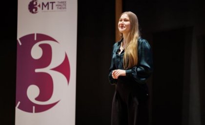 A woman with blonde hair wearing a green blouse and navy pants standing on a stage